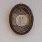 Antique mother of pearl button in an oval frame with ribbon going through it