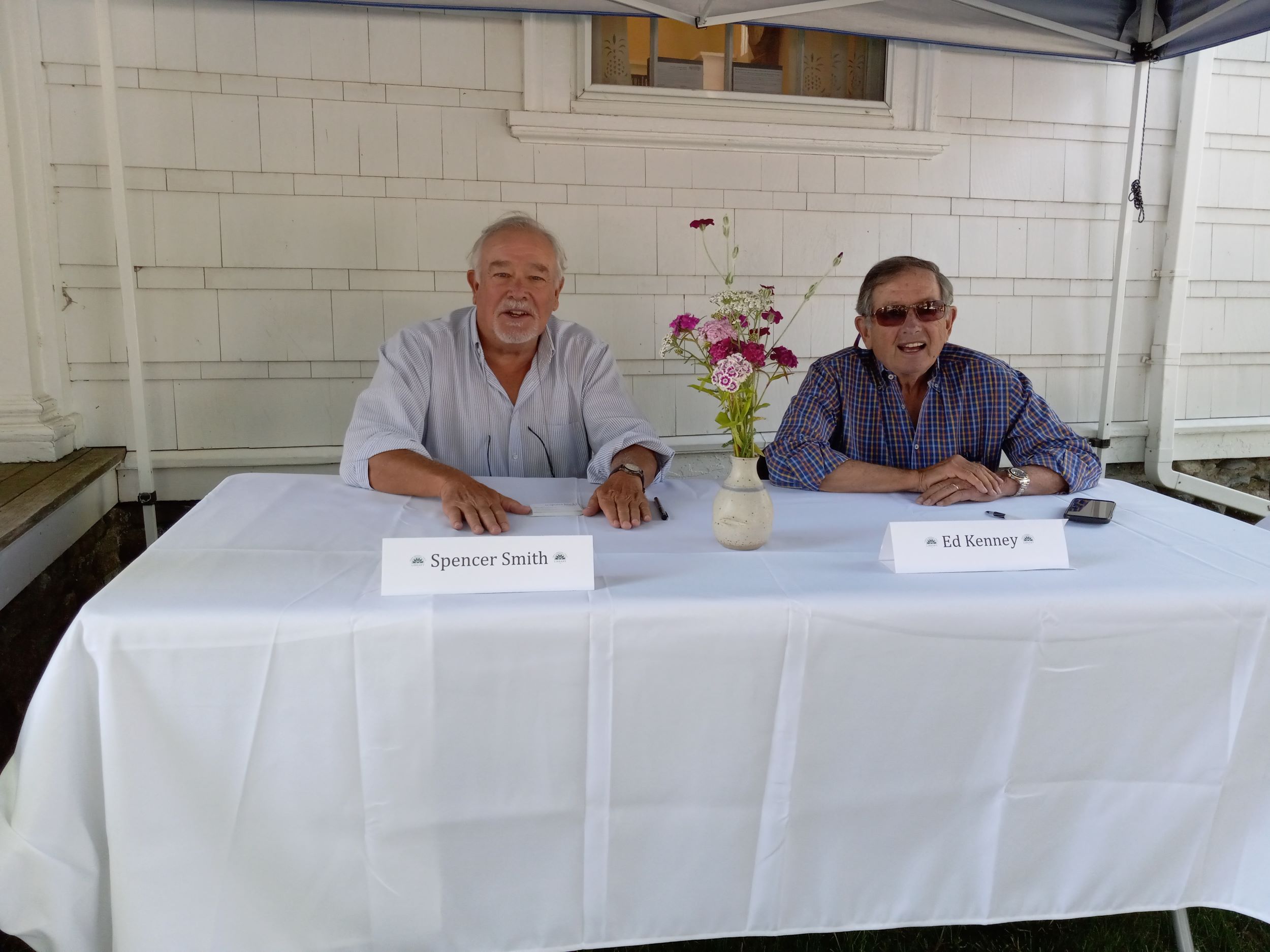 Publisher Spencer Smith sitting at white table with author Ed Kenney at an  outdoor Friend Memorial Library event